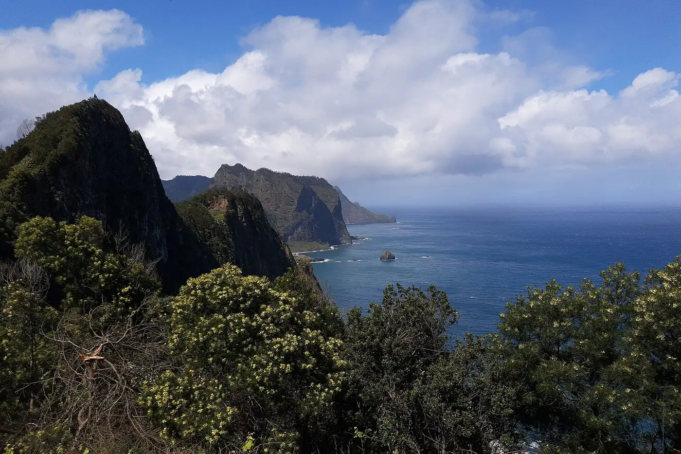 Dark volcanic peaks and green slopes on the northern coast of Madeira under white clouds