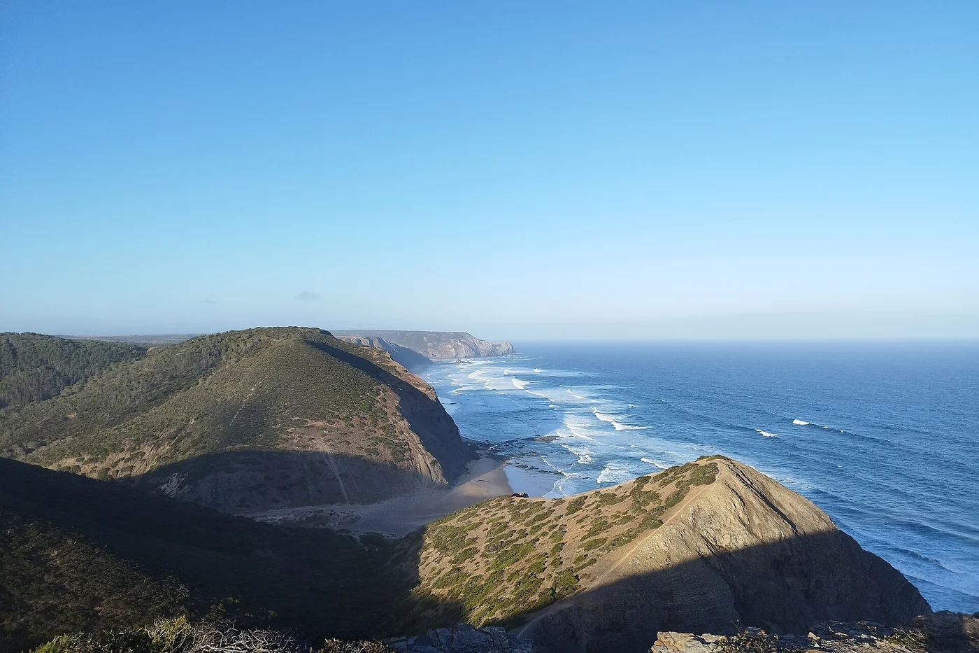 Green hills and a quiet beach on the wild Costa Vicentina, with the Atlantic stretching to the horizon